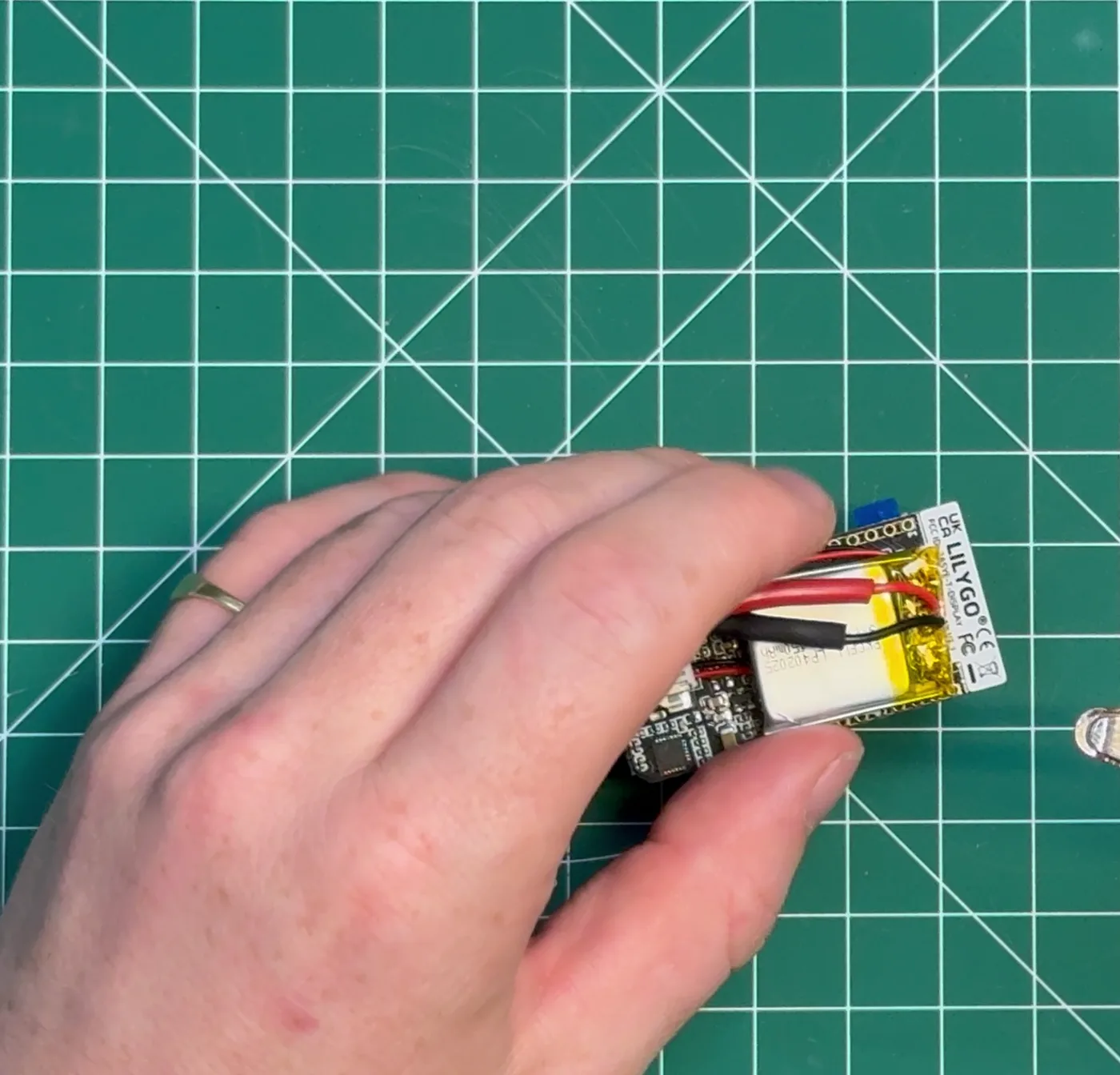 Placing the LiPo battery flat against the back of the board with tweezers.