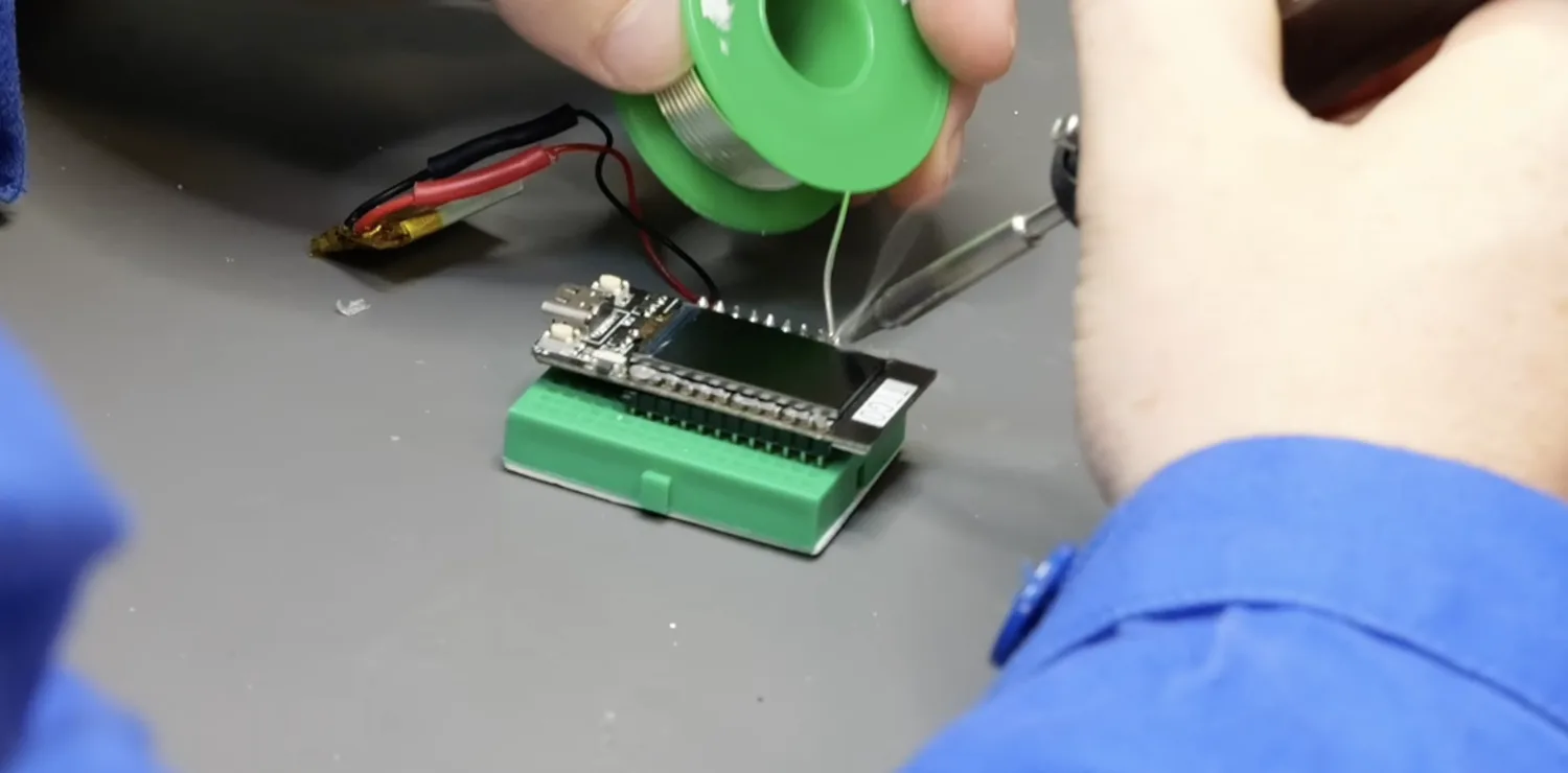 Soldering header pins into the T-Display while a breadboard holds it square on the bench.