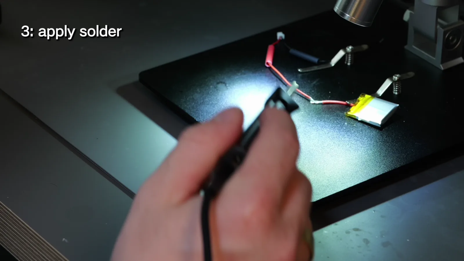 Soldering the battery wires under a microscope, iron tip on the joint.