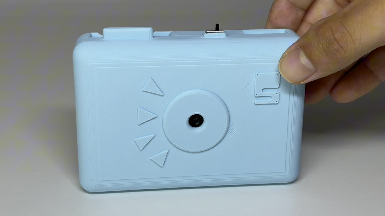 The camera half: a 3D-printed shell with the lens in the middle and the power switch on the top edge.